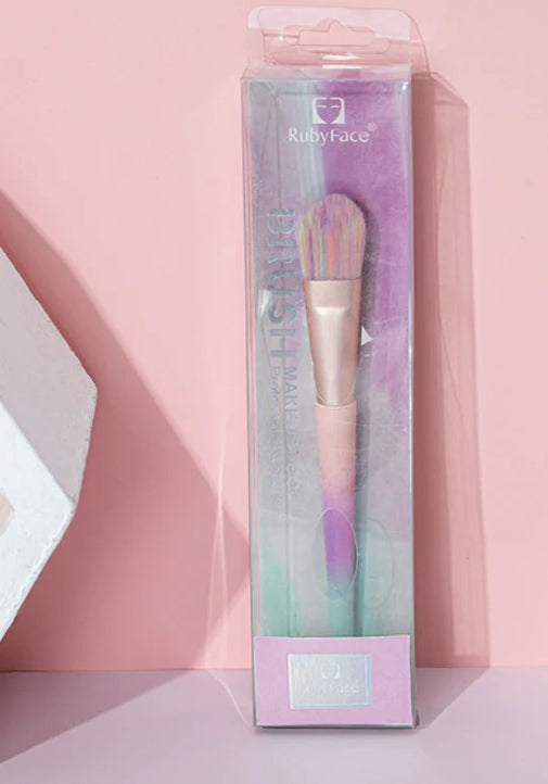 Pastel unicorn bronzer brush with wooden handle in clear packaging against a pink background