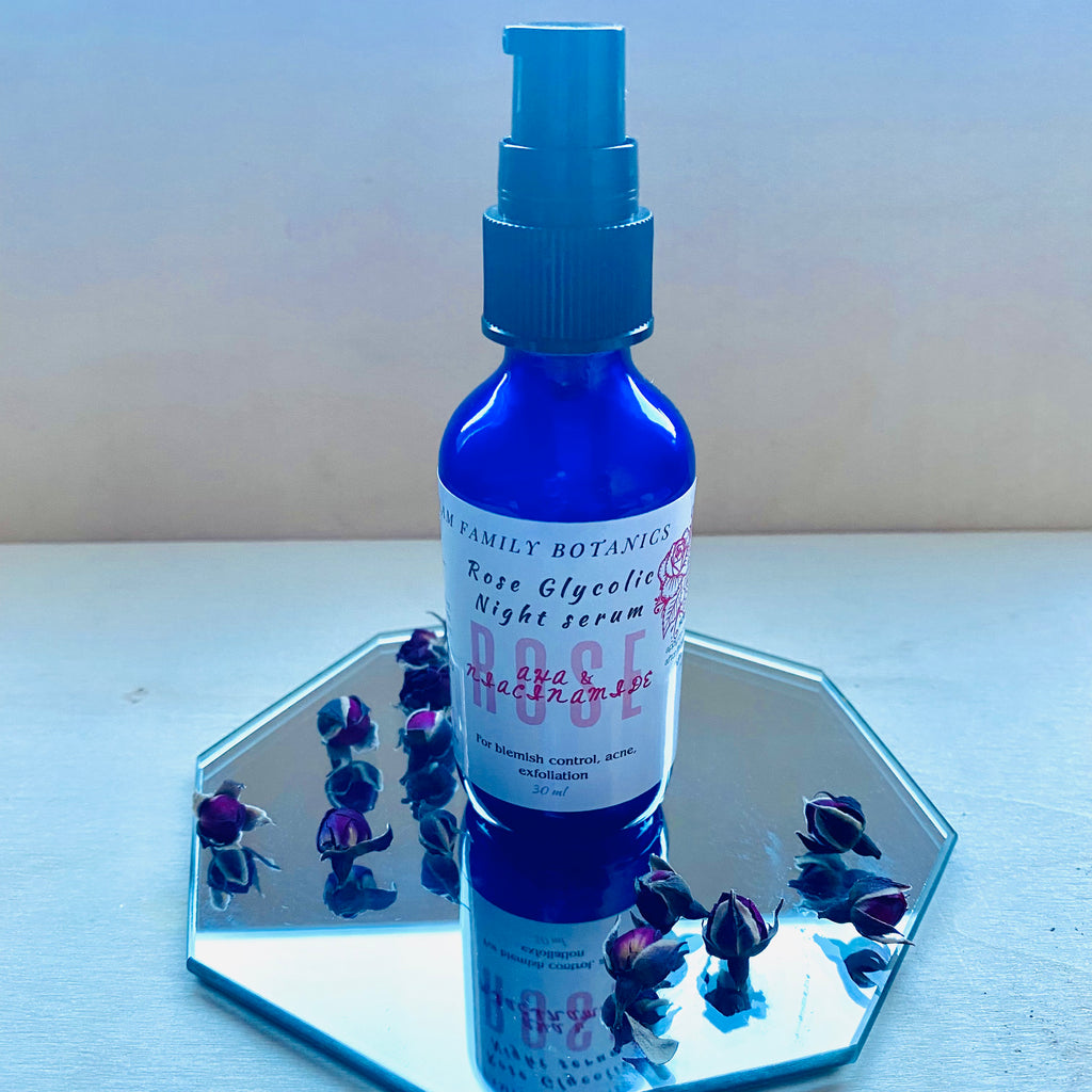 Blue bottle of Rose Glycolic Night Serum on a hexagonal mirror with dried rosebuds around it