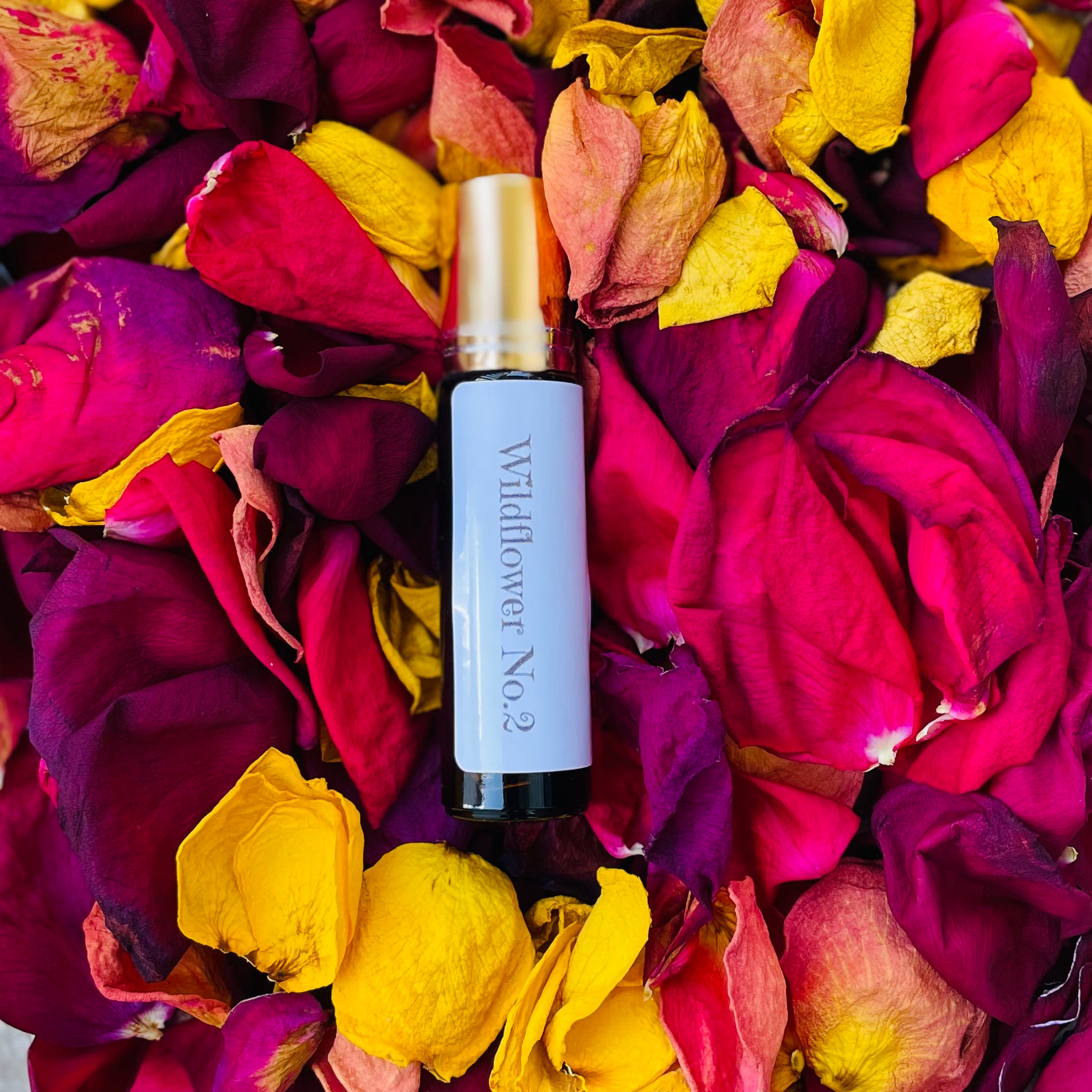 Wildflower No.2 perfume oil rollerball surrounded by vibrant red, yellow, and purple dried flower petals.